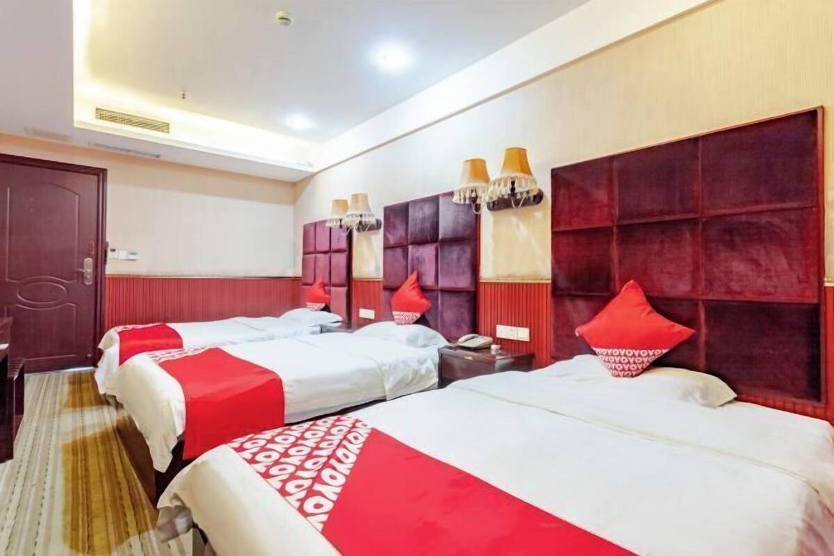 Een hotelkamer met drie bedden, elk met rode en witte beddengoed, en een groot, rood hoofdeinde.