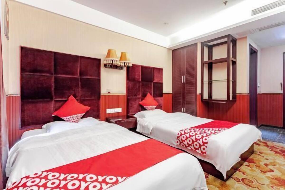 Een hotelkamer met twee bedden, rood-witte beddengoed, een groot houten hoofdeinde, een kledingkast en een kamerbreed tapijt met dessin.