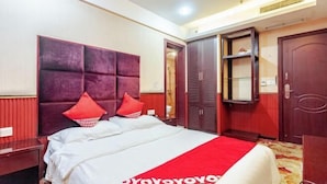 Una habitación de hotel con una cama grande, ropa de cama roja y blanca, una almohada decorativa roja, un armario y un estante pequeño.
