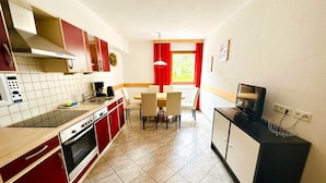 A compact kitchen with red and white cabinets, a microwave, a coffee maker, and a dining area with a table and chairs. - Apartment in Fugen Near Ski Lift (Fuegen)