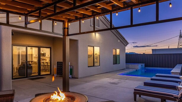 Un patio al aire libre con una fogata, sillones de descanso y una piscina.