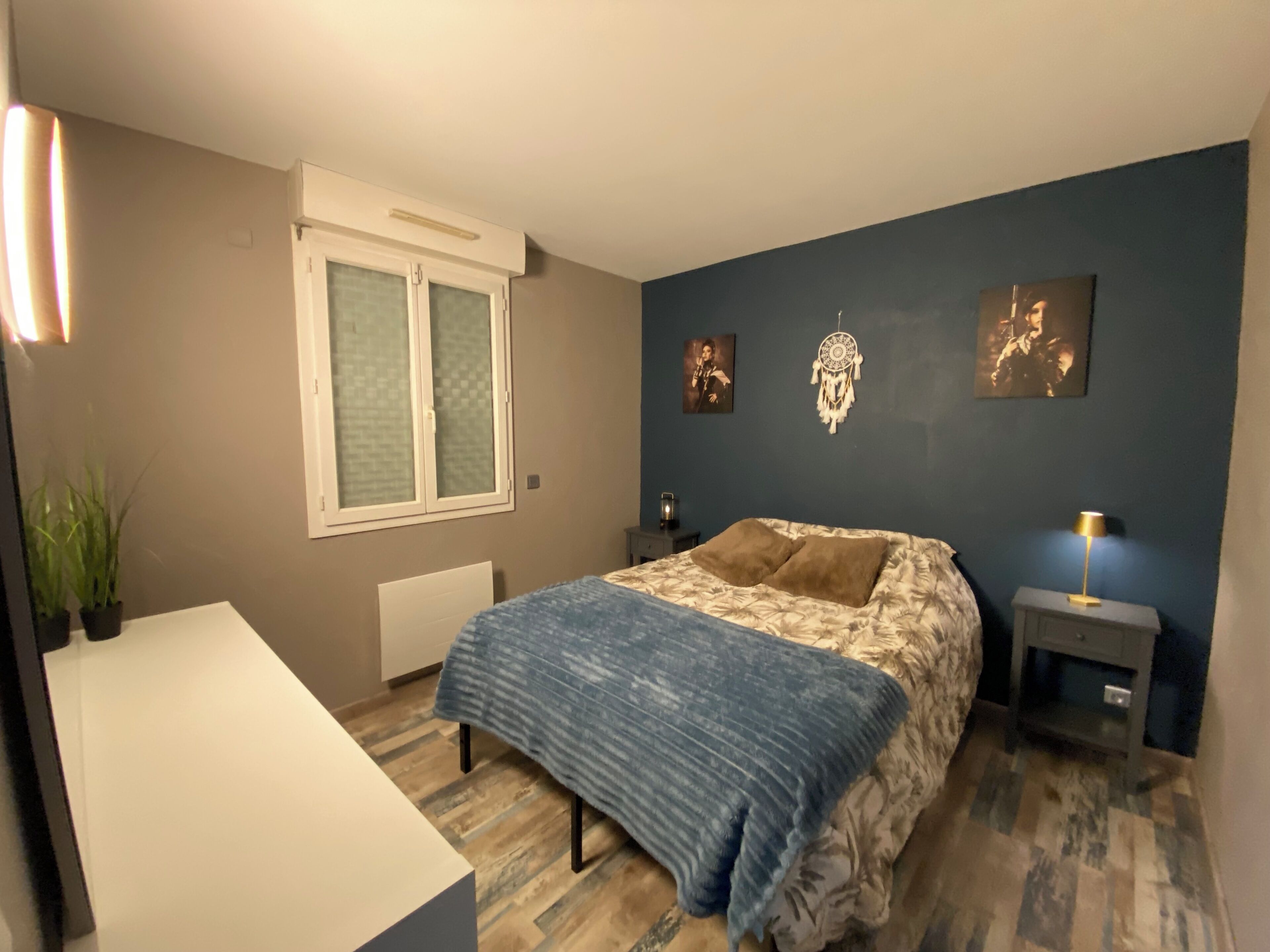 Un dormitorio con cama, mesitas de noche, radiador, ventana y decoración en la pared.