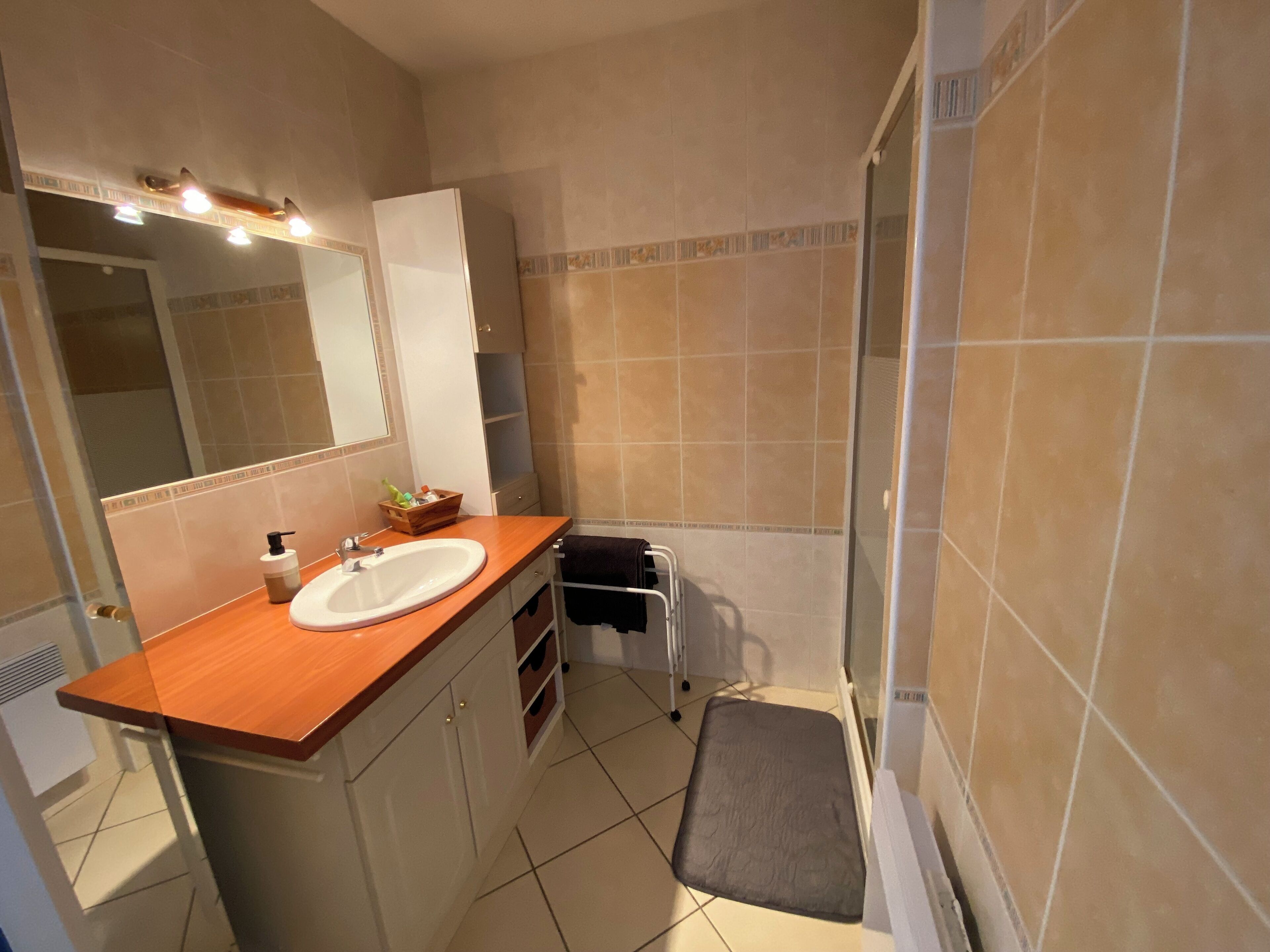 Un baño con tocador de madera, lavamanos blanco, espejo y zona de ducha.