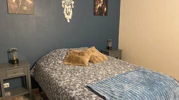 A bedroom with a floral-patterned bedspread, two pillows, a blue blanket, a dreamcatcher, and two wall-mounted pictures.