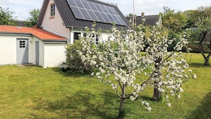 A house with a sloped roof, solar panels, and a garden with blooming trees.