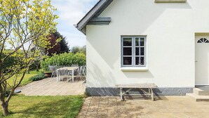 A white house with a paved patio, a wooden bench, and a white door.