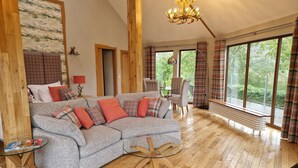 A spacious living room with a grey sofa, plaid cushions, a glass coffee table, and a wooden floor. - Luxury, secluded, Adult only Treehouse with hot tub, woodburner & stunning views (Glenshee)