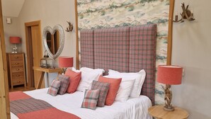 A bedroom with a large bed, a wooden headboard, a wall tapestry, a dresser, a mirror, and a bedside table with a lamp. - Luxury, secluded, Adult only Treehouse with hot tub, woodburner & stunning views (Glenshee)