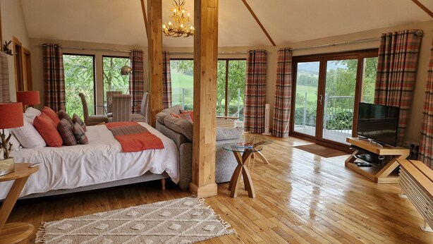A spacious bedroom with a large bed, a sitting area with a glass table, and a TV. - Luxury, secluded, Adult only Treehouse with hot tub, woodburner & stunning views (Glenshee)