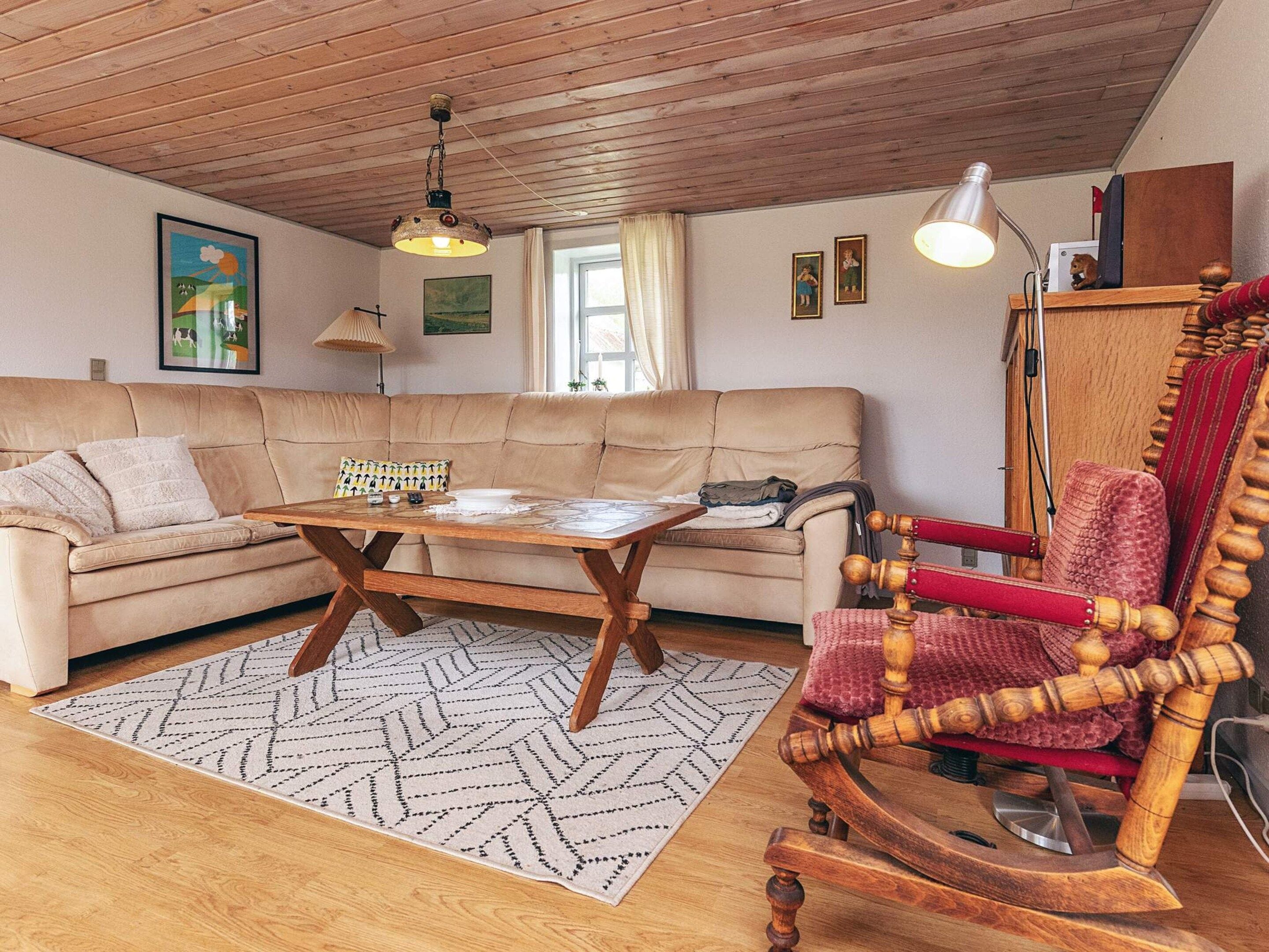 Un salón acogedor con un sofá, una mesa de centro de madera, un sillón mecedor y una alfombra estampada.