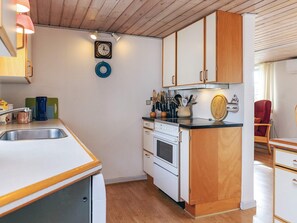 Een functionele keuken met houten kastjes, een spoelbak, een kookplaat en een klok aan de muur.