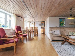 A spacious living area with wooden flooring, a sofa, a dining table with chairs, and a kitchen in the background.