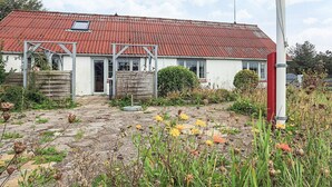 Een gelijkvloers huis met een rode pannendak, een veranda met een houten poort en een kleine tuin met diverse planten en bloemen.