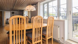 Een eetruimte met een houten tafel en stoelen, grote ramen en een plafond met houten balken.