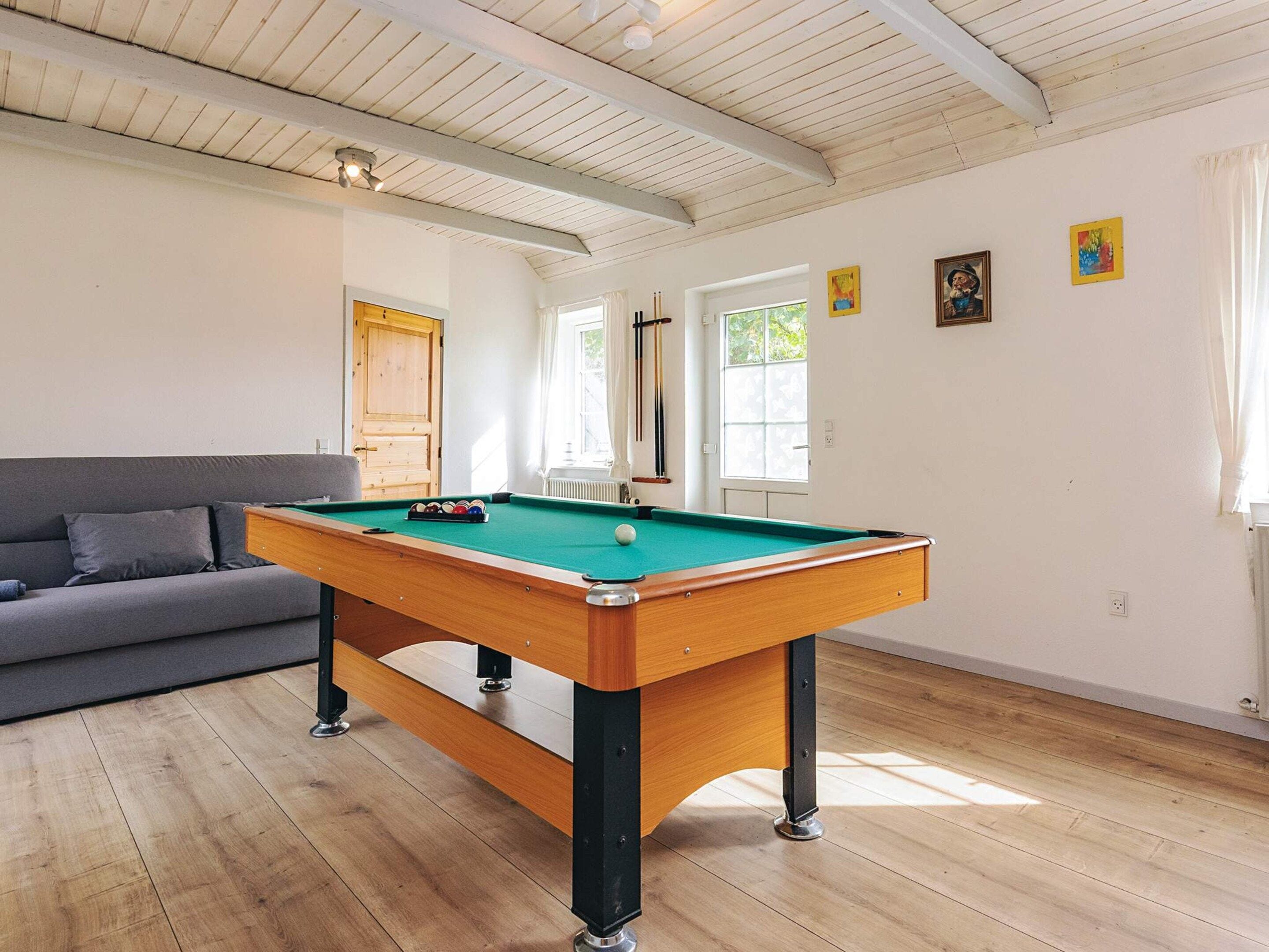 Une table de billard dans une pièce dotée d’un plancher en bois, d’un canapé et d’une porte.