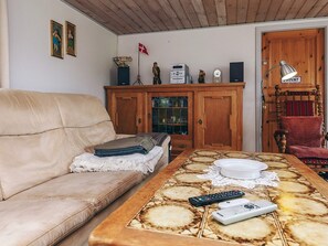 Een woonkamer met een bank, een houten kast, een tafeltje met een kantborduurwerk en een rode fauteuil.