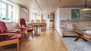 Een ruime woonkamer met houten vloer, een bank, een eettafel met stoelen en een keuken in de achtergrond.