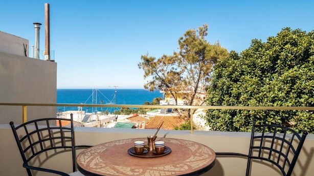 A balcony with a round table, two chairs, and a view of the sea and buildings. - Danae's House Elegant Residence in  Chalepa, Chania (Chania)