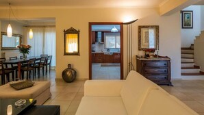 A living room with a sofa, a coffee table, a dining area with chairs, a kitchen visible through an open door, and a staircase. - Danae's House Elegant Residence in  Chalepa, Chania (Chania)