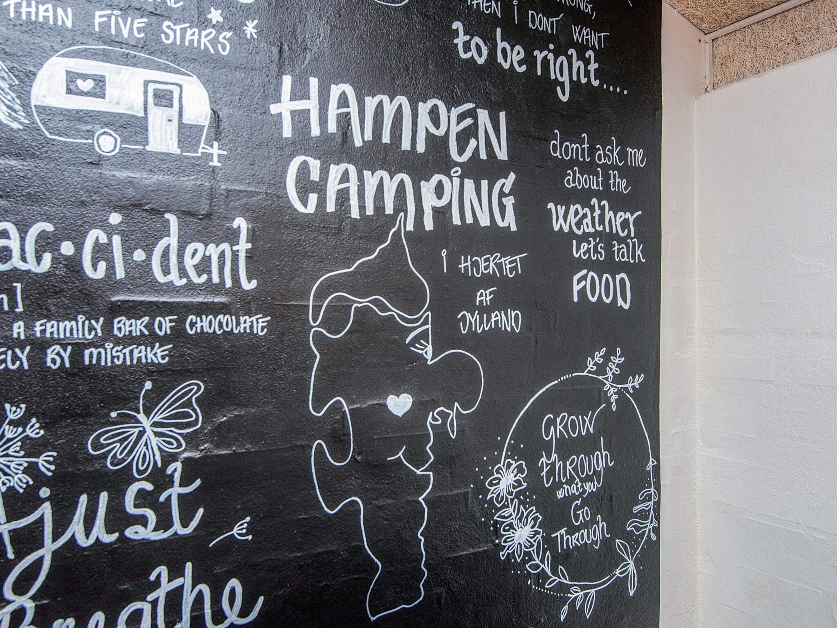 Un tableau noir sur lequel on peut voir diverses phrases et dessins griffonnés, notamment « Happen Camping », « Une tablette de chocolat pour toute la famille » et « Respirez simplement ».