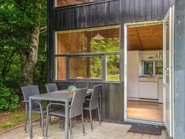 Uma área moderna para refeições ao ar livre, com mesa e cadeiras, uma janela grande e vista para uma cozinha.