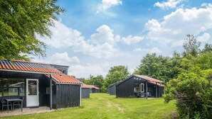 A row of rustic cabins with metal roofs, surrounded by lush greenery and a clear sky.