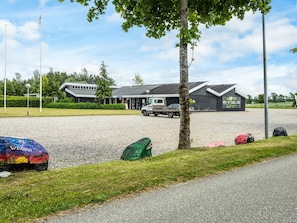 Un espace de stationnement recouvert de gravier, avec un bâtiment en arrière-plan, un camion garé devant et un arbre sur la gauche.