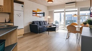 A modern kitchen with wooden cabinets, a white refrigerator, and a dining area with a sofa and table. - 4 Person Holiday Home in Vestervig (Vestervig)