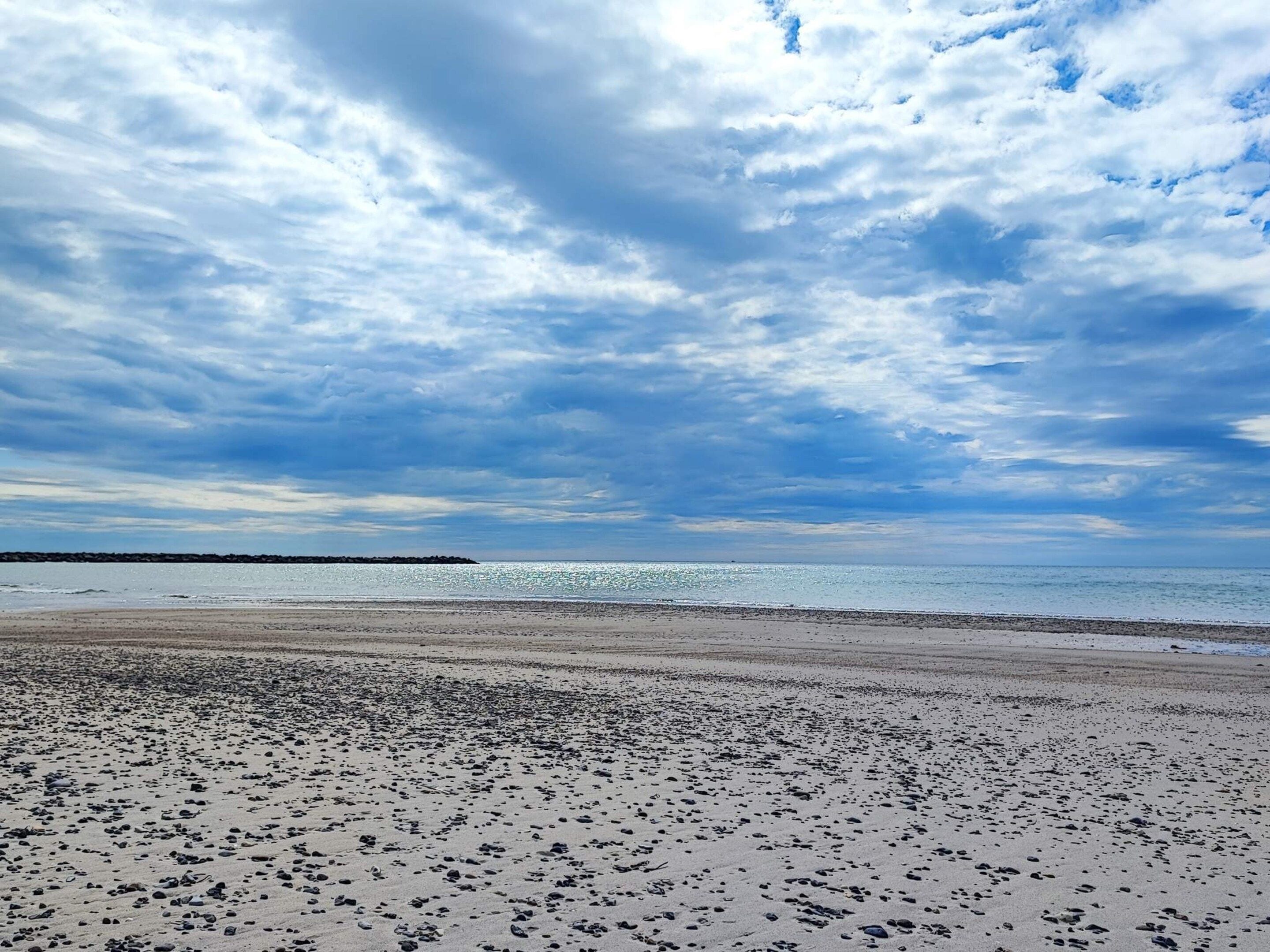 Une plage avec une vaste étendue de sable et une mer calme sous un ciel partiellement nuageux.