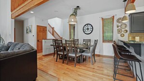A dining area with a wooden table and chairs, a kitchen with a bar, and a staircase. - Ultimate Group Stay, Pickelball, H/Tub, Fire Pit (Lake Harmony)
