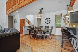 A dining area with a wooden table and chairs, a kitchen with a bar, and a staircase.