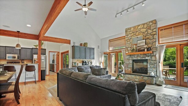 A spacious living area with a stone fireplace, a large sofa, and a dining area with wooden beams and a ceiling fan. - Ultimate Group Stay, Pickelball, H/Tub, Fire Pit (Lake Harmony)