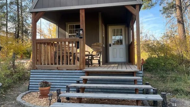 Een houten hut met een veranda, een deur en een kleine tafel met stoelen.