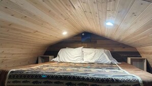 Een knus slaapkamer op zolder, met schuine wanden, een bed met een beddeken met dessin en een klein dakvenster.