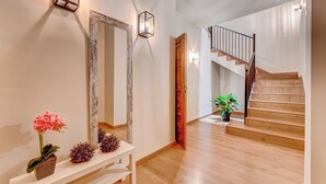 A spacious hallway with a wooden staircase, a white console table with decorative plants, and wall-mounted sconces.