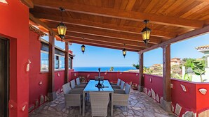 A covered outdoor seating area with a stone floor, red walls, and a view of the sea.