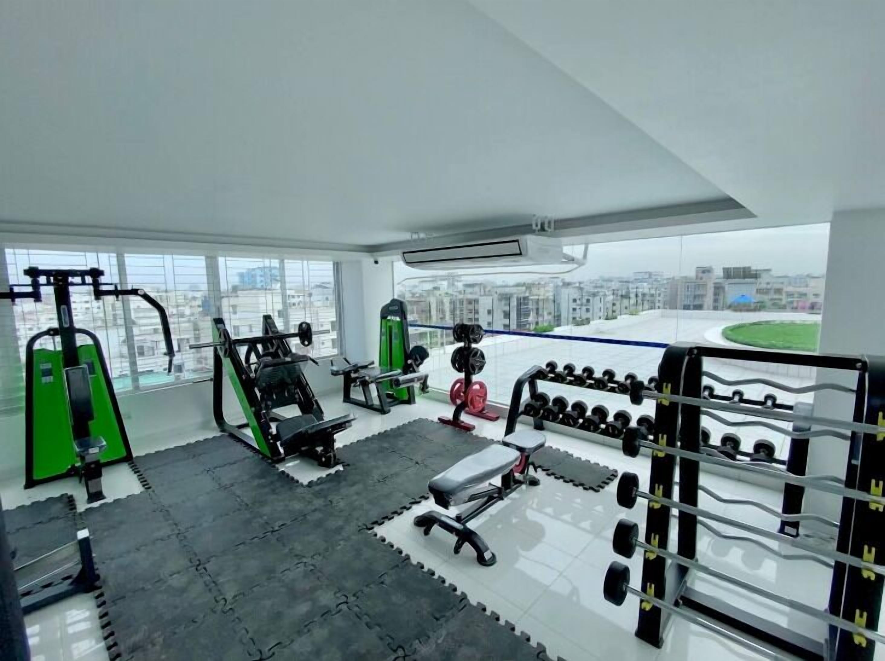 Ein Fitnessraum mit verschiedenen Trainingsgeräten, darunter Kraftgeräte, Kurzhanteln und eine Bank.