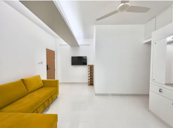 Una habitación moderna y minimalista con un sofá blanco, un televisor de pantalla plana montado en la pared y un ventilador de techo.