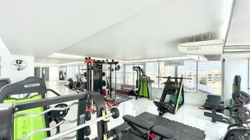 A gym with various exercise equipment, a bench, and a large window offering a view of the city.