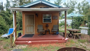 A wooden cabin with a porch, two chairs, a table, and a swan decoration.