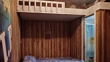 Habitación pequeña con literas, paredes de madera, una alfombra estampada y una escalera.