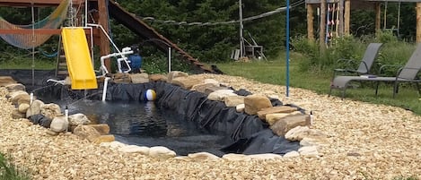 A playground with a slide, a small water feature, and a seating area with chairs.