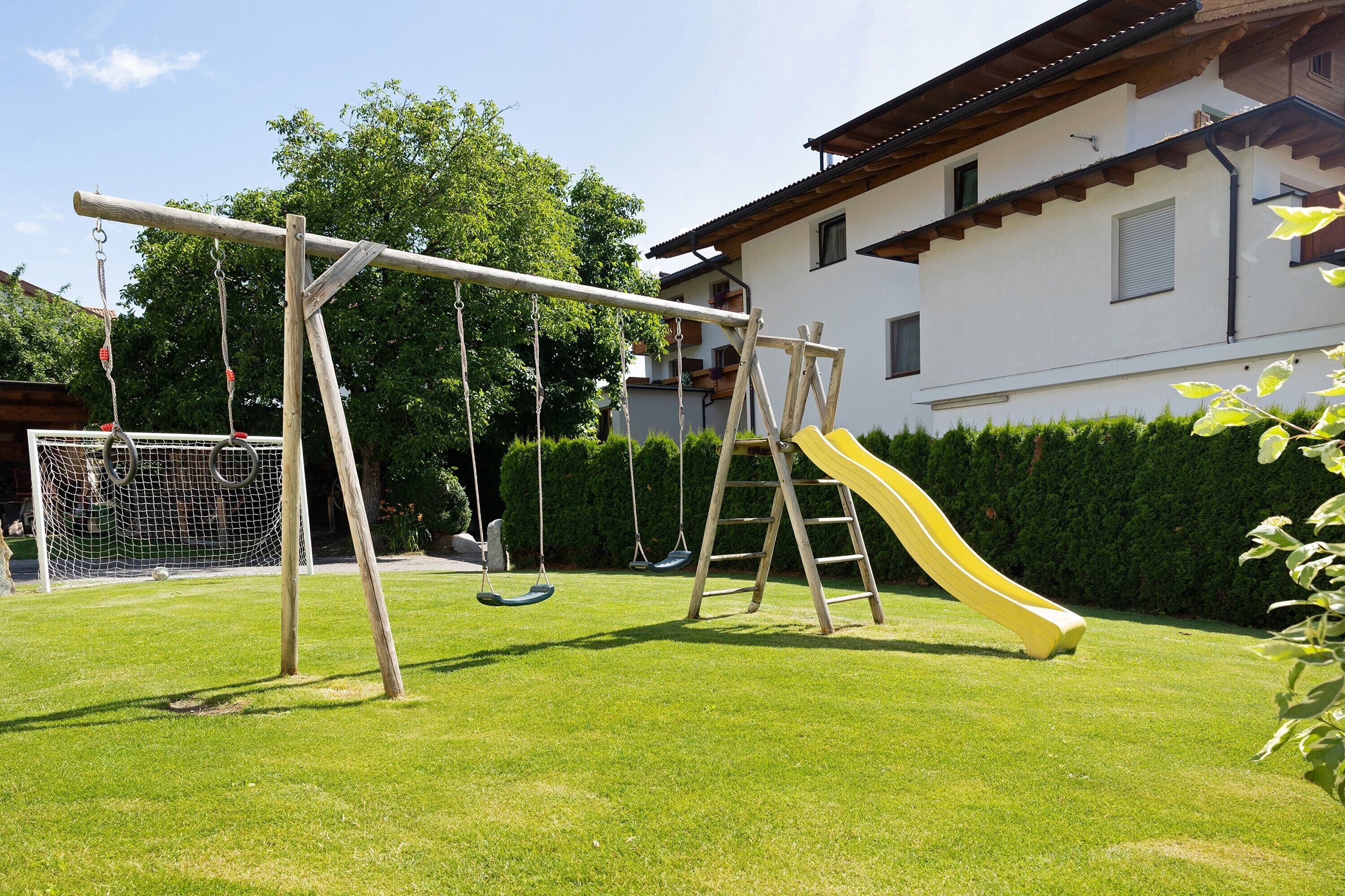 A playground with swings and a slide, a soccer goal, and a building with a balcony in the background.