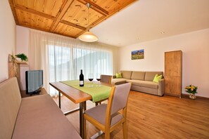 Un salon avec un plafond en bois, un canapé, une table à manger recouverte d’une nappe verte, un téléviseur et un meuble.