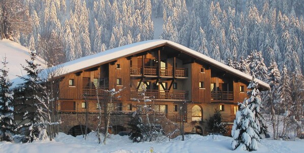 A wooden lodge with multiple balconies, surrounded by snow-covered trees.