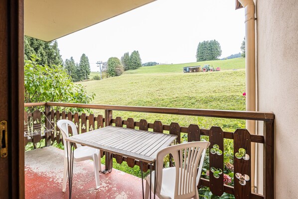 A balcony with a table and chairs, a wooden fence, and a view of a green field with a tractor.