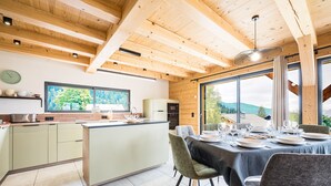 A modern kitchen with wooden beams, a dining area with a table set for four, and large windows offering a view of the outdoors.