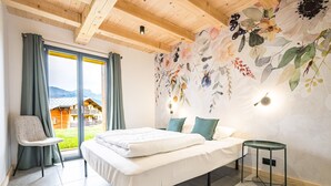 A bedroom with a bed, a chair, a small table, and a wall with floral wallpaper.