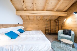 Soqquadro in legno, un letto con lenzuola bianche e azzurre, una sedia, un tavolino e una scala.