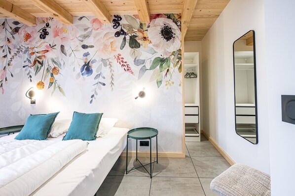 Une chambre à coucher avec un lit, deux oreillers, une petite table, un miroir et une décoration murale à motifs floraux.